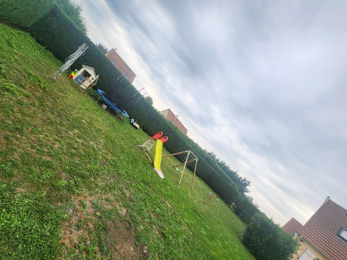 Vue d'un jardin familial avec haie taillée et jeux pour enfants